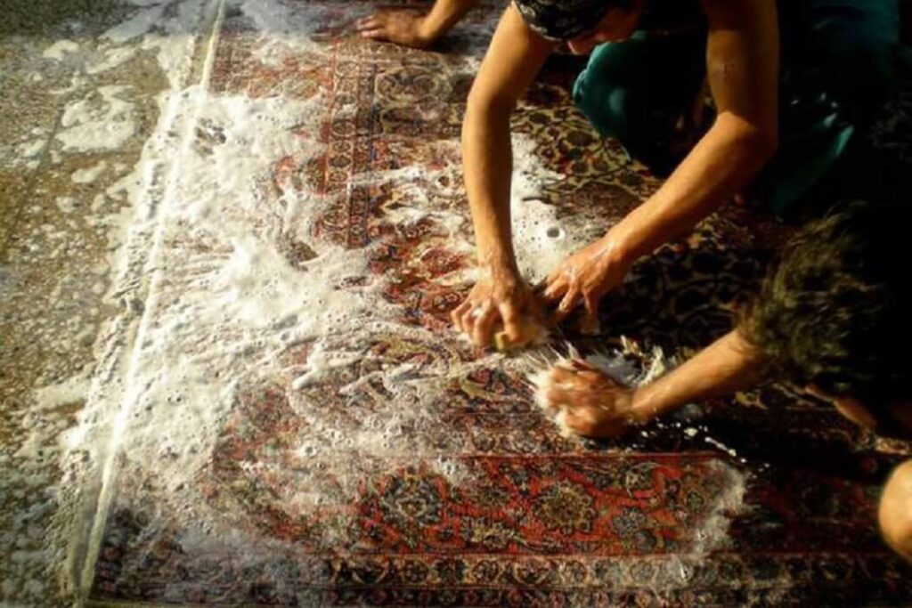 چنتا مرد در حال شستشوی فرش با دست توی یه قالیشویی غرب تهران ، روی قالی کلی کف مالیده شده و دارن با اسکاج و دست روشو تمیز میسابن