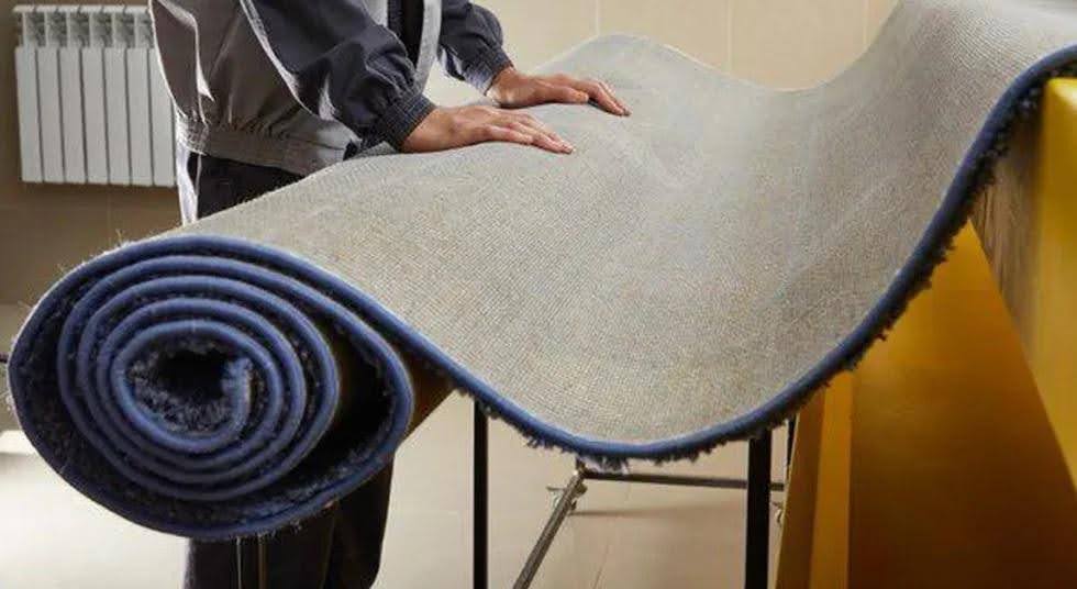 یه مرد با لباس کار در قالیشویی که دستش روی یه قالی شسته شده توی قالیشویی جنوب تهرانه و فرش شسته شده در حال خشک شدن روی یک چهارپایه آهنیه